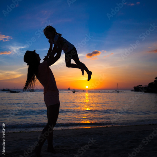 Silhouette of mother and little daughter playing on the beach of
