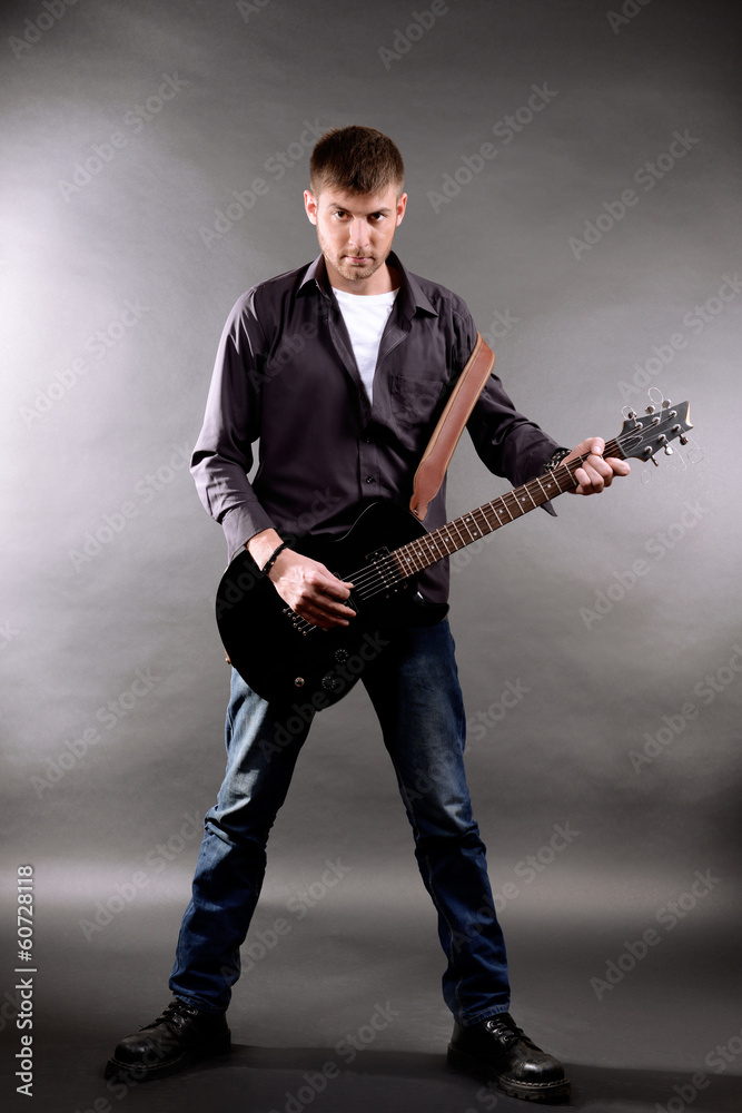 Fototapeta premium Young musician playing guitar on gray background