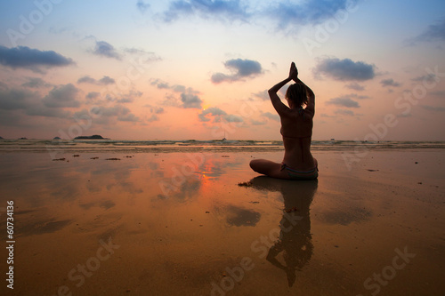 Silhouette young woman practicing yoga on the sea beach