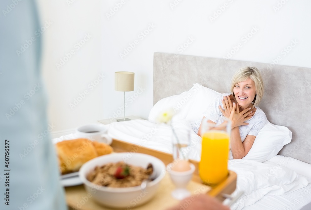 Happy woman sitting in bed with breakfast in foreground Happy woman sitting in bed with breakfast in foreground