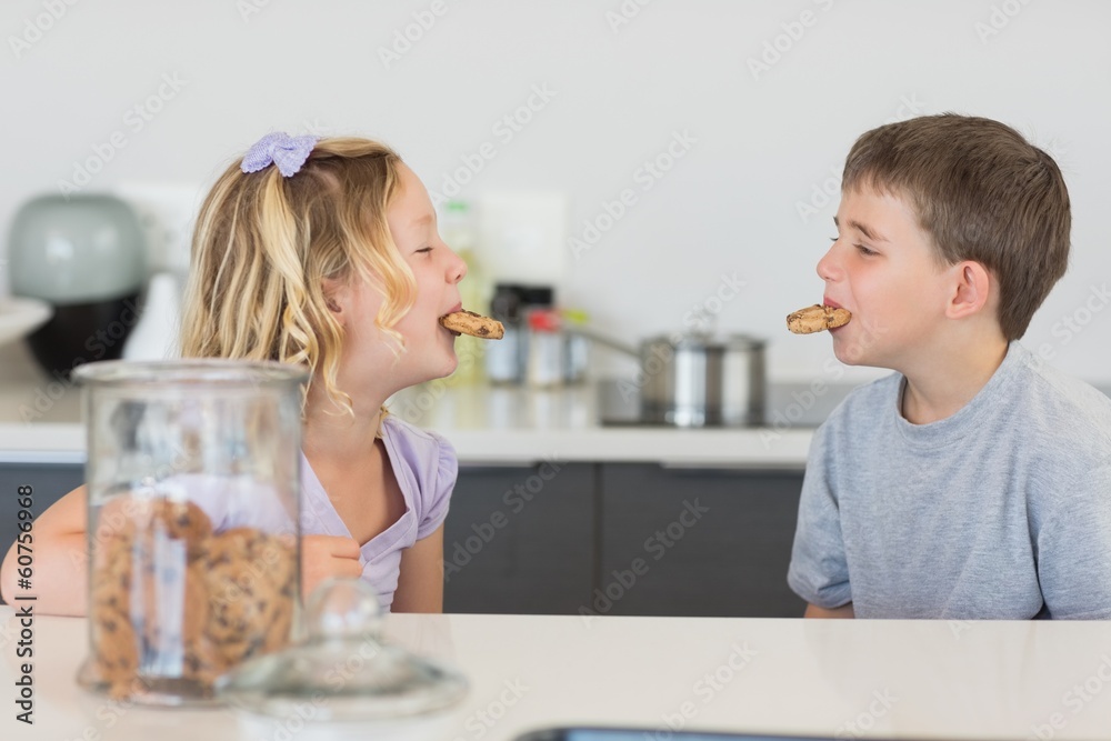 Siblings with cookies in mouth at kitchen counter Siblings with cookies in mouth at kitchen counter