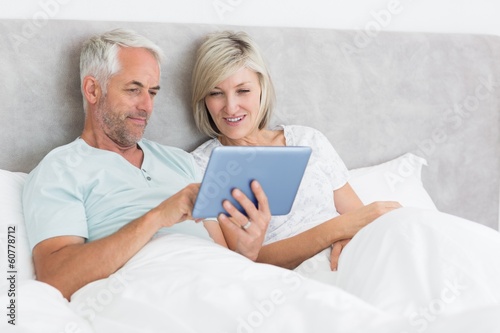 Happy couple using digital tablet in bed