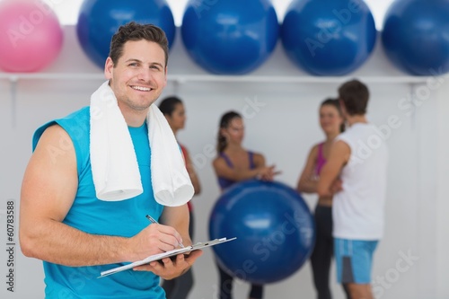 Male trainer holding clipboard with fitness class in background
