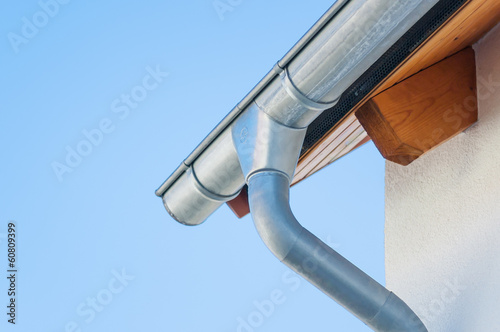 Corner of a house with gutters on a background of blue sky