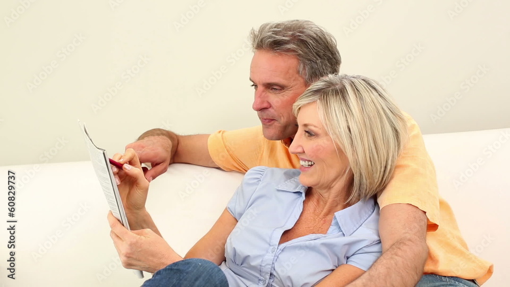 Couple laughing together on the couch doing the crossword puzzle Stock