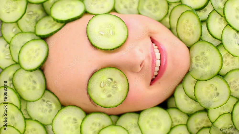 Smiling womans face surrounded by cucumber slices