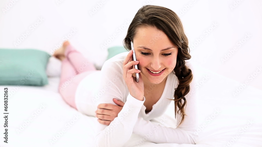 Smiling woman lying on bed chatting on the phone Smiling woman lying on bed chatting on the phone