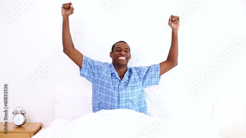 Happy man yawning and stretching sitting in bed