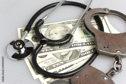 Stethoscope, handcuffs and money on gray