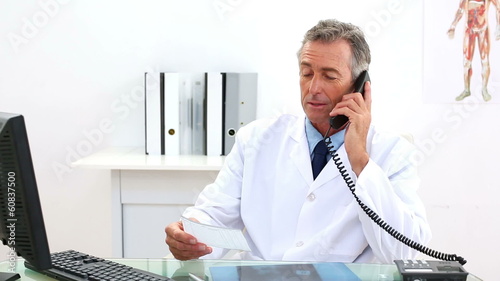 Mature doctor talking on the phone at his desk