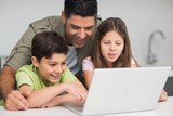 Father with young kids using laptop in kitchen