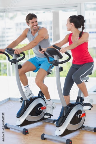 Fototapeta Naklejka Na Ścianę i Meble -  Smiling young couple working out at spinning class