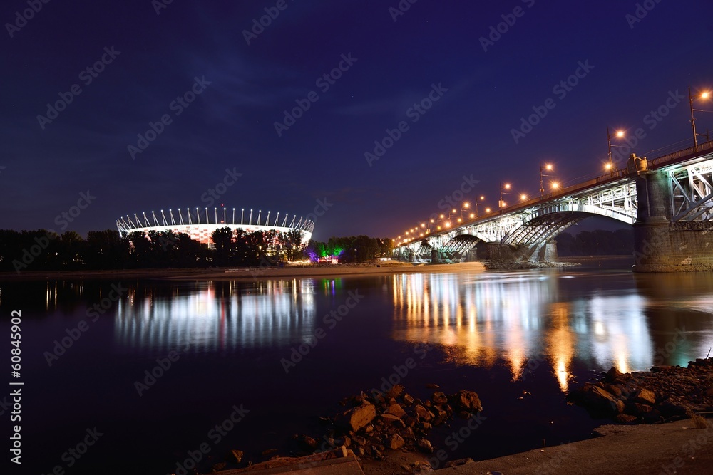 Obraz premium Most Poniatowskiego i Stadion Narodowy w Warszawie nocą.