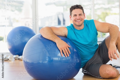 Smiling young man sitting with fitness ball at gym