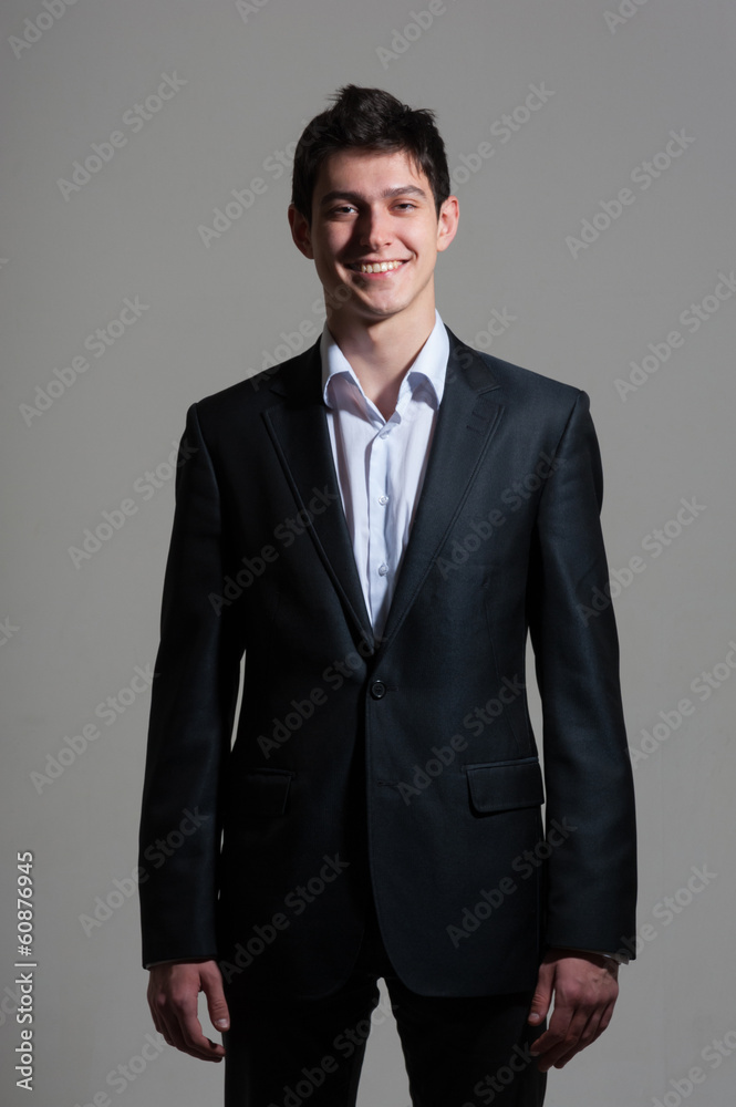 Fototapeta premium Portrait of young smiling handsome business man in suit on grey