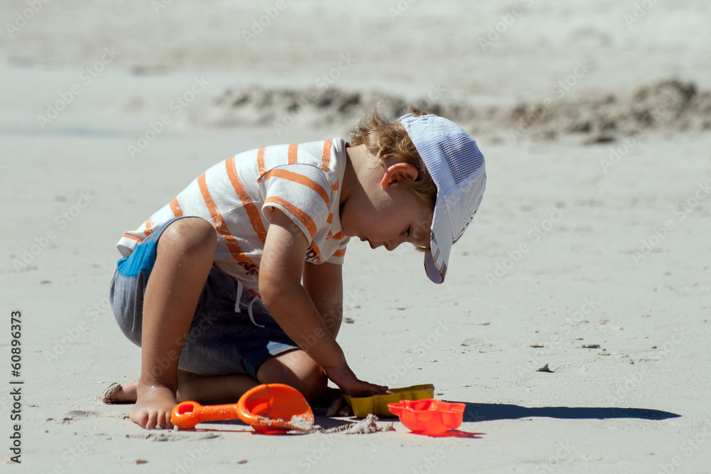 A little boy is preparing to build a sand castle on a beach
