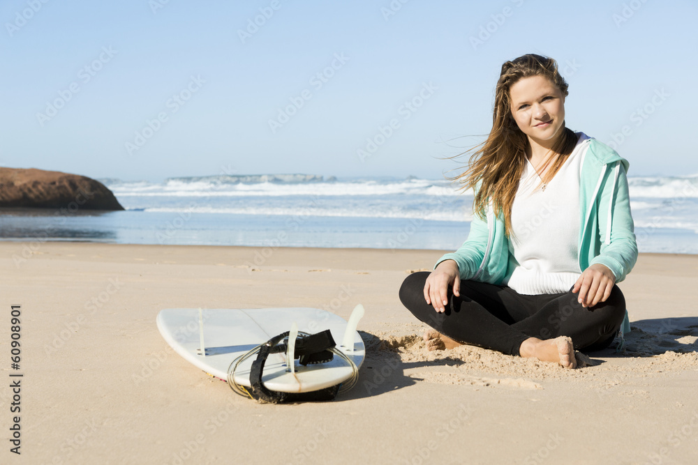 Fototapeta premium Teenage surfer girl sitting in the beach with her surfboard