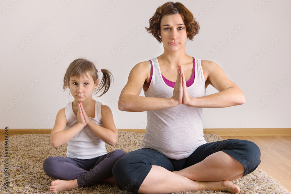 Pregnant woman and little daughter yoga exercising Pregnant woman and little daughter yoga exercising