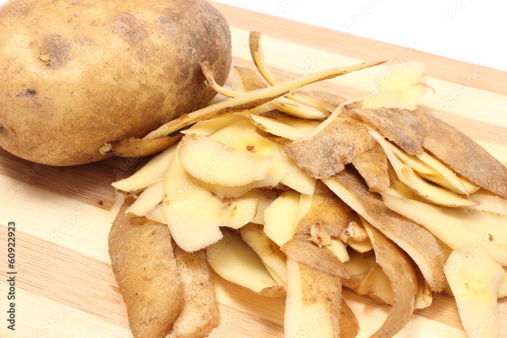 Whole potato and peels lying on wooden cutting board
