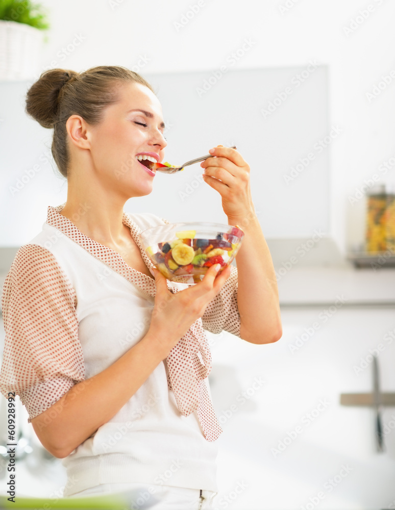 Happy young housewife eating fresh fruit salad in kitchen Happy young housewife eating fresh fruit salad in kitchen