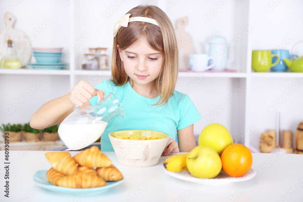 Beautiful little girl eating breakfast in kitchen at home