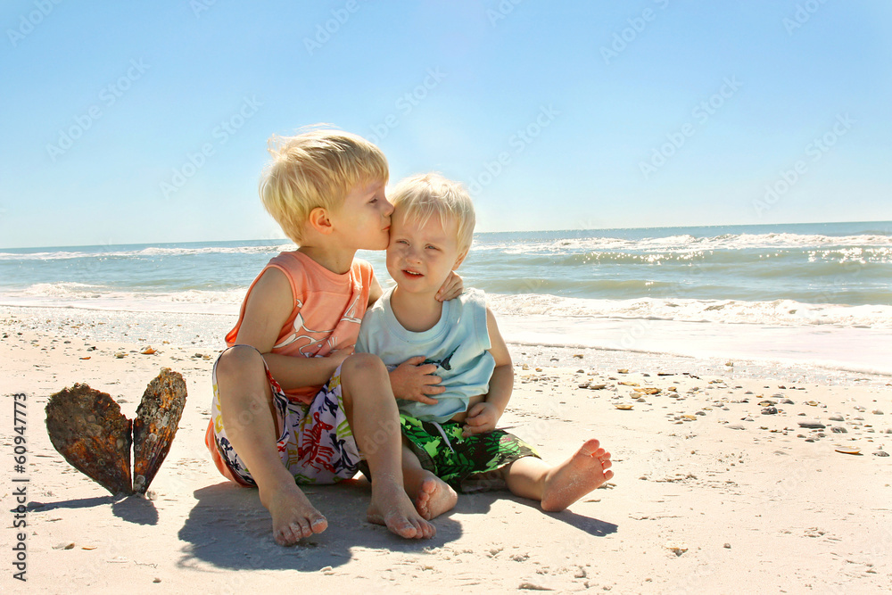 Big Brother Kissing Baby as they Sit on the Beach by the Ocean Big Brother Kissing Baby as they Sit on the Beach by the Ocean