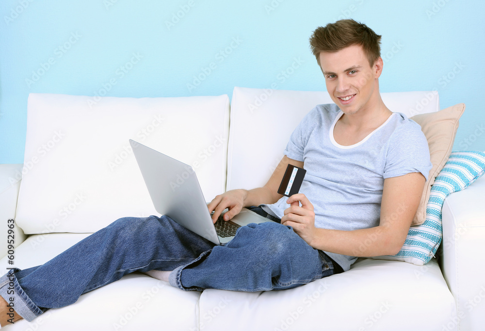 Guy lie on sofa with laptop on blue background Guy lie on sofa with laptop on blue background