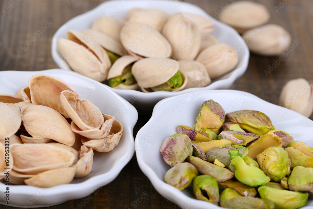 Pistachio nuts in small bowls on wooden background