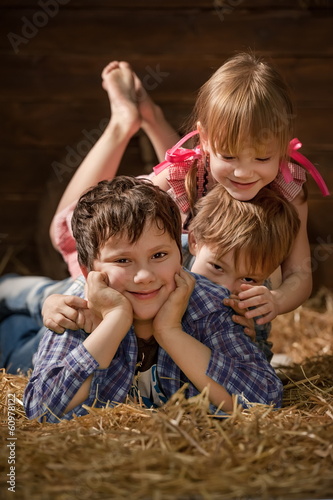 Three laughing children on hay in a hangar
