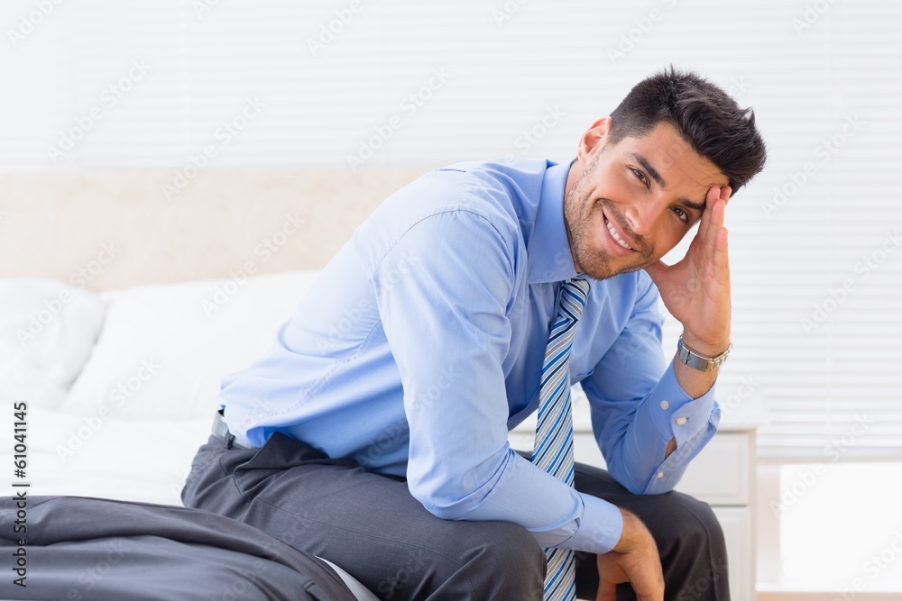 Cheerful businessman sitting at edge of bed looking at camera