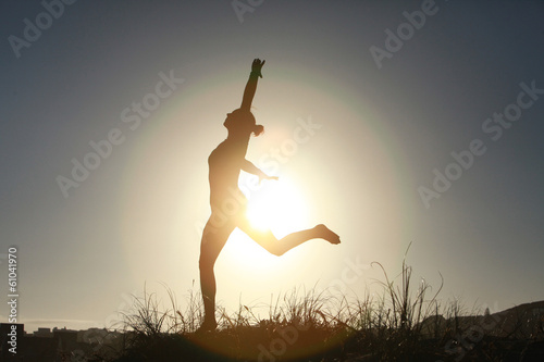 Silhouette of acrobatic teen gymnast balancing with the sun behi
