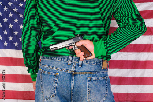 Man holding a 1911, 45 ACP behind his back in front of an American flag photo