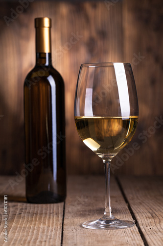 Black bottle of wine and wineglass on the wooden background .
