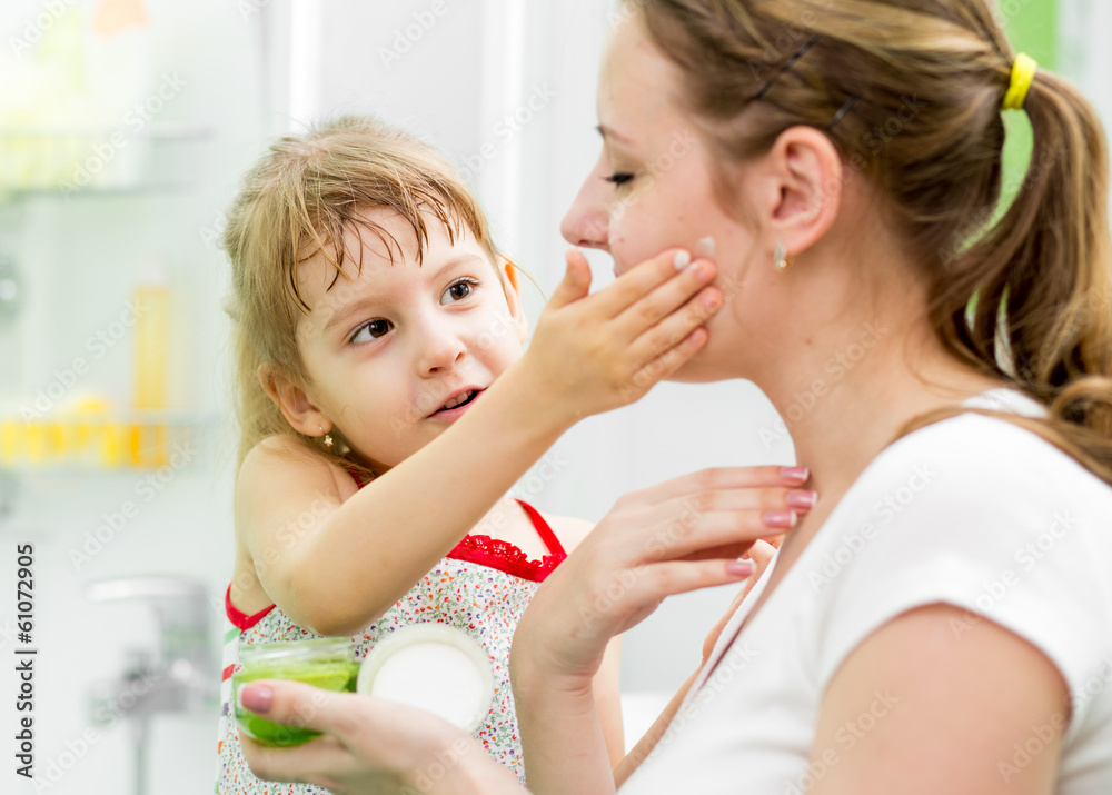 kid daughter putting cream on her mother's face in bathroom