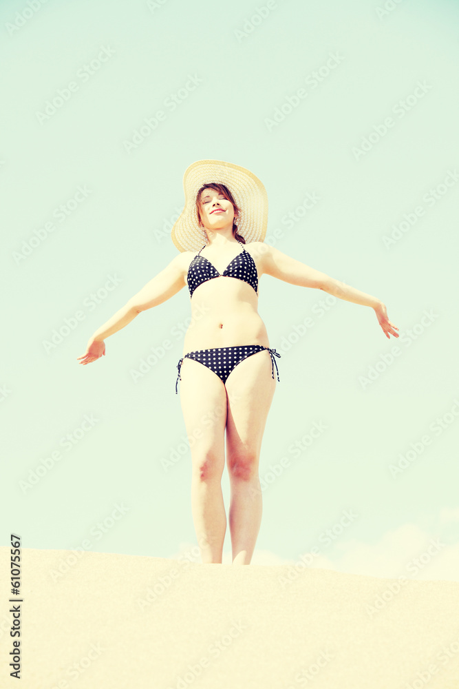 Young woman standing on beach in bikini and straw hat. Young woman standing on beach in bikini and straw hat.