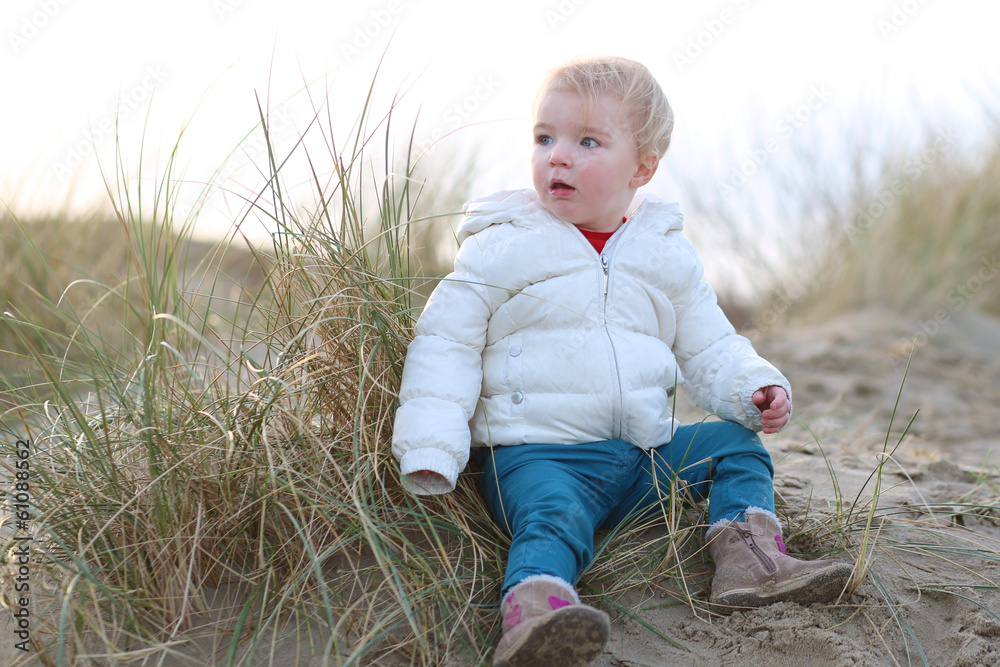 Cute toddler girl in warm white coat plays in winter dunes Cute toddler girl in warm white coat plays in winter dunes