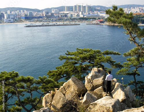 korean man standing on rocks looking at city view