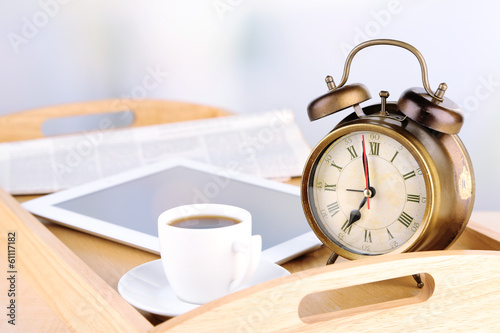 Tablet, newspaper, cup of coffee and alarm clock on wooden tray