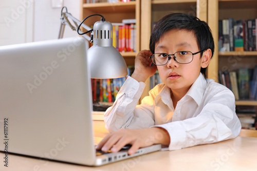 Intelligent boy wearing glasses working on laptop computer