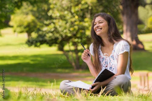 Young woman with book and pen sitting in park