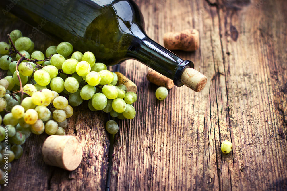 Obraz premium Bottle of white wine, grape and corks on wooden table