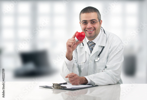 Doctor sitting at his desk with stethoscope holding heart