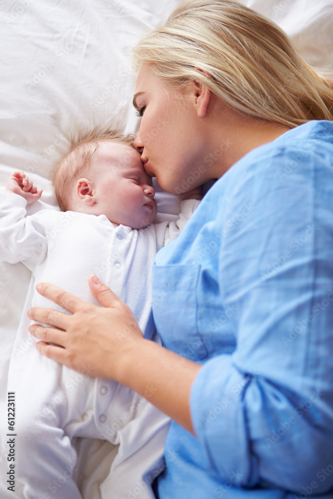 Mother Kissing Baby Girl As They Lie In Bed Together