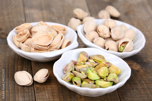 Pistachio nuts in small bowls on wooden background