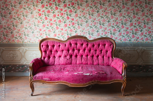 Old damaged red couch in an antique house. Flowers wallpaper