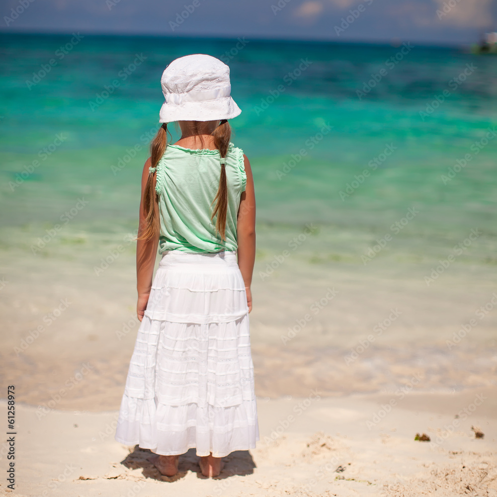 Rear view of little girl in hat looking at the sea on white sand