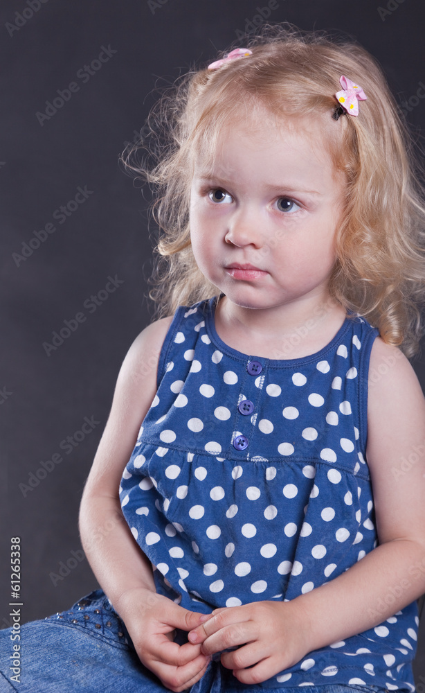 Naklejka premium serious little girl 3 years old, on dark background.