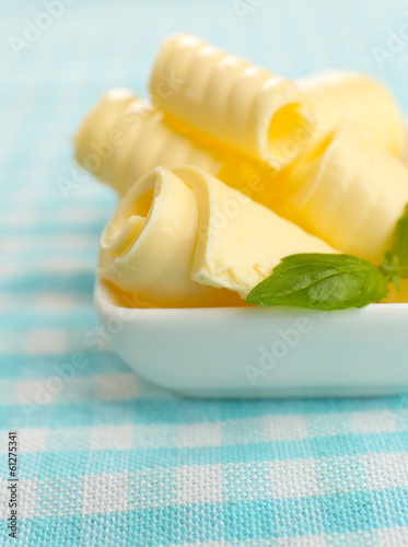 Curls of fresh butter with basil in bowl, on blue tablecloth