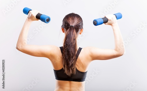 Fit woman during exercise with dumbbells, back view