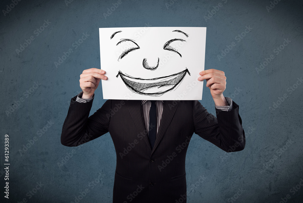 Businessman holding a paper with smiley face in front of his hea Businessman holding a paper with smiley face in front of his hea
